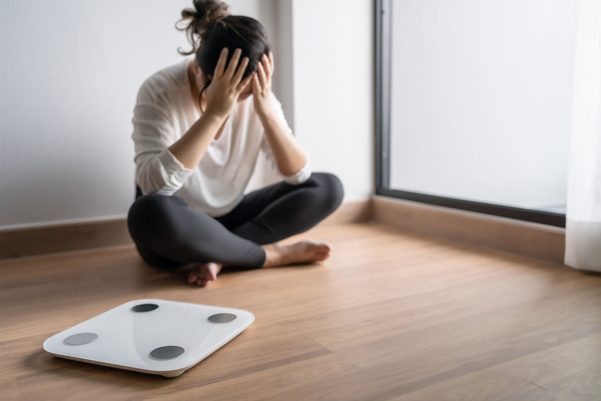 Woman sitting on the floor with her hands on her face and a Weight Scale